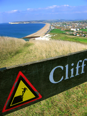 Cliff warning sign with Seaford beach in background